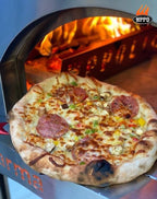 Finished pizza on a peel in front of the WPPO Karma 32 wood-fired oven with flames burning inside