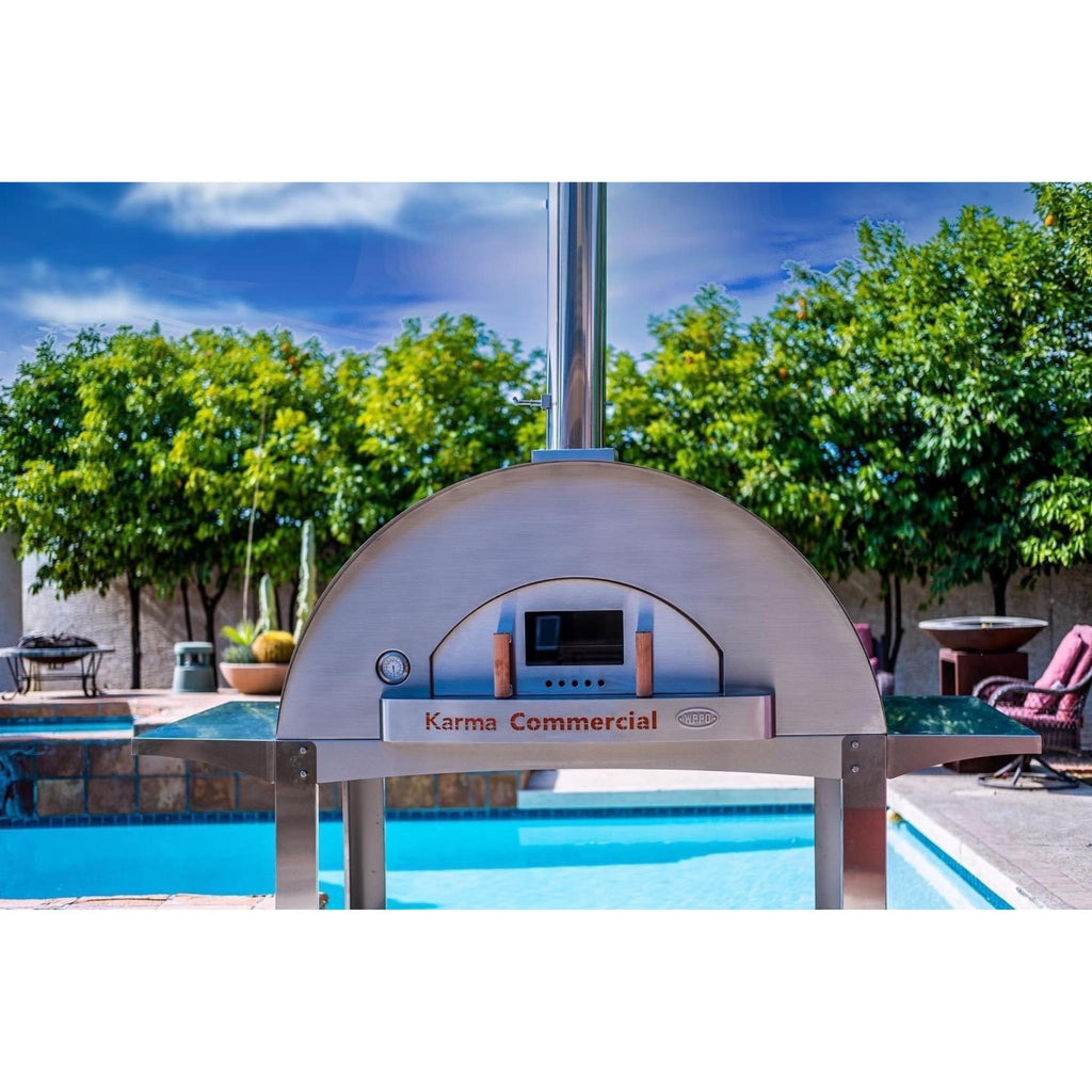 WPPO Karma 55 Commercial wood-fired oven on its stainless stand beside a pool, with stack and door temperature gauge