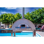 WPPO Karma 55 Commercial wood-fired oven on its stainless stand beside a pool, with stack and door temperature gauge